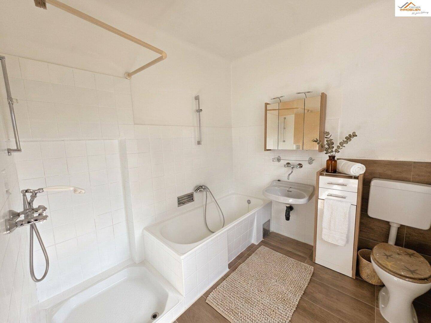 Badezimmer mit Badewanne, Dusche, Waschbecken und WC, ausgestattet mit weißen Fliesen und Holzdetails.