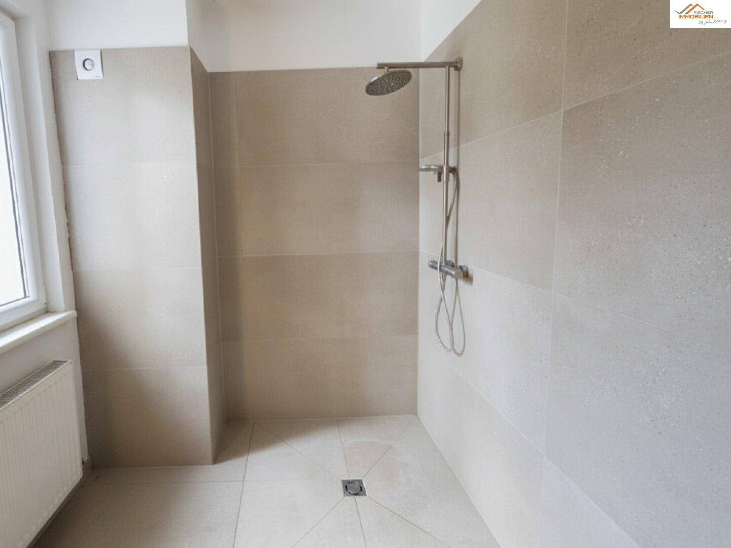 Modern geflieste Dusche mit Regenduschkopf und großformatigen Fliesen in neutralem Farbton.