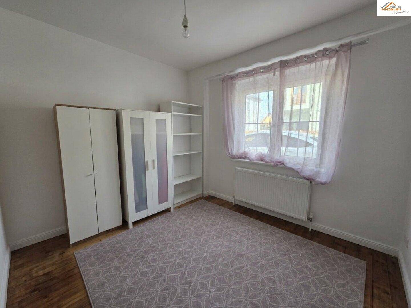 Schlafzimmer mit Teppichboden, Kleiderschränken und einem Fenster mit Vorhängen.
