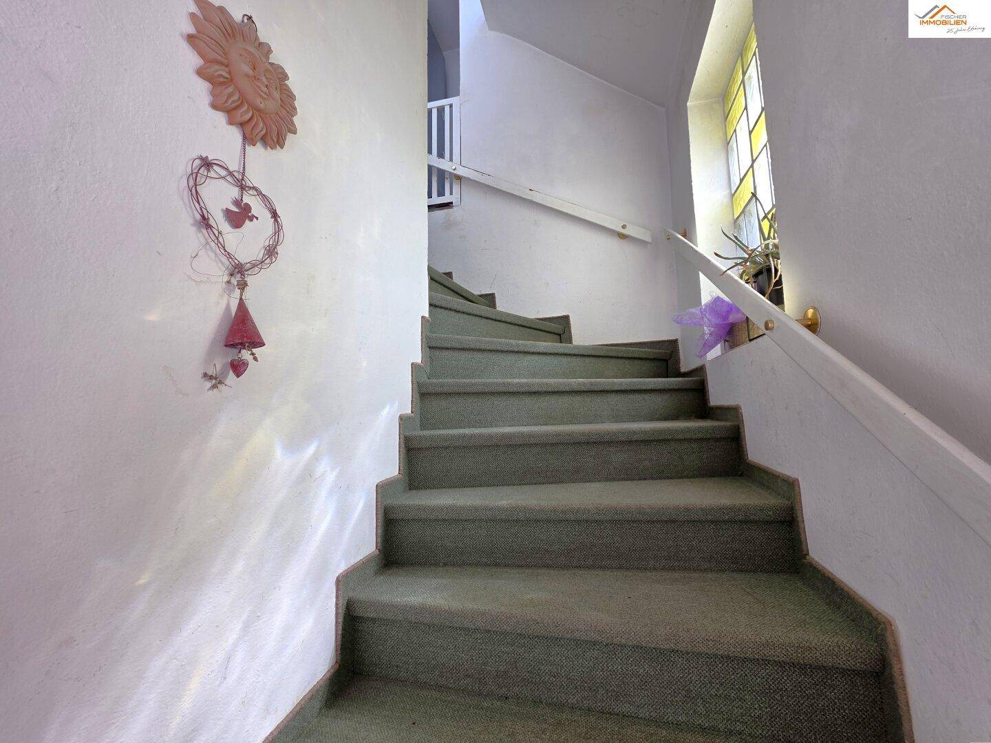 Treppenhaus mit Teppichboden und einem farbigen Glasfenster, das für natürliches Licht sorgt.