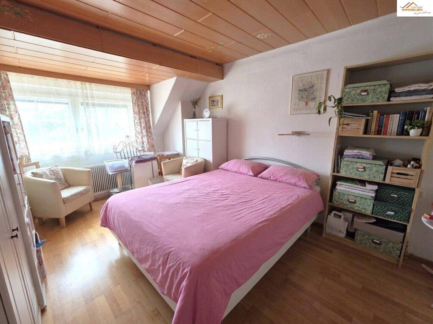 Schlafzimmer mit Doppelbett, Holzdecke und Fenster, das viel Tageslicht hereinlässt.