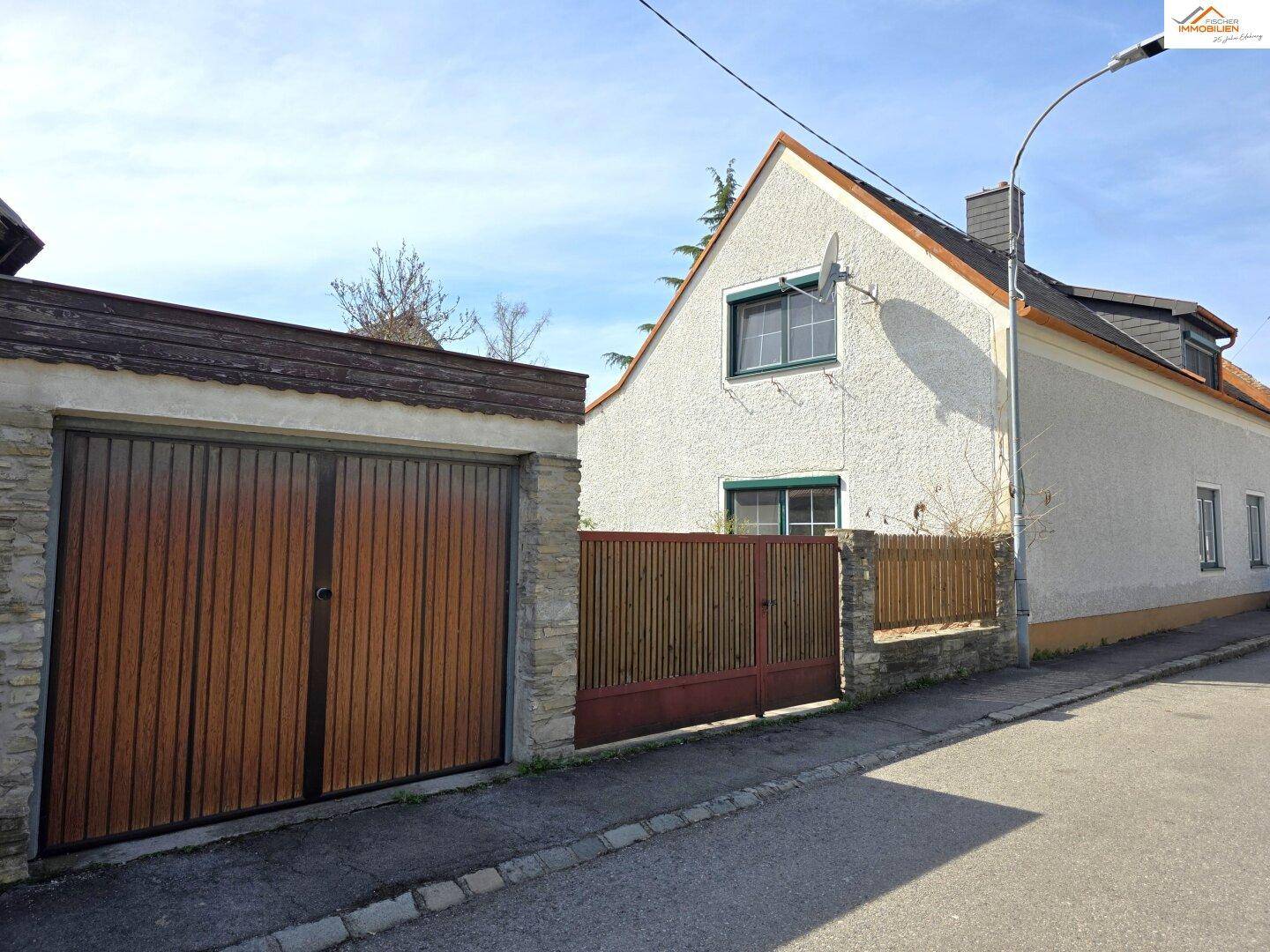 Ansicht des Hauses von der Straße mit Garage und Einfahrtstor an einem sonnigen Tag.