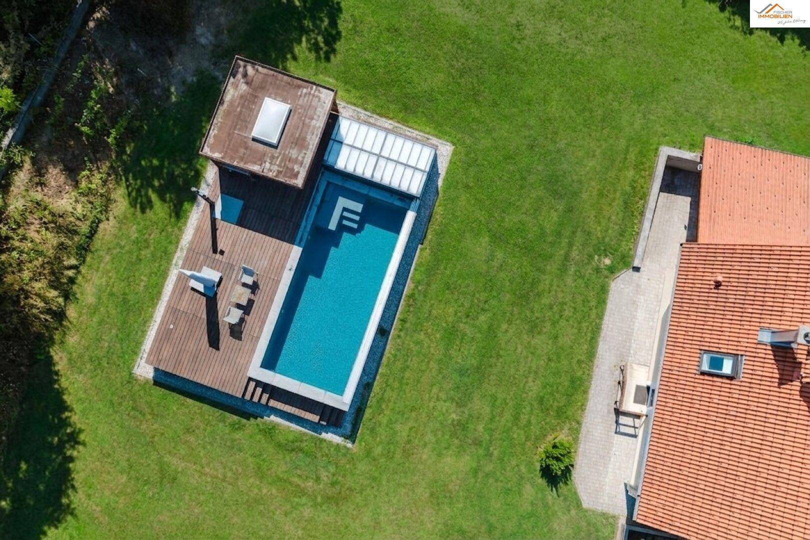 Blick von oben auf den modernen Swimmingpool mit Holzdeck und Poolhaus im Garten.