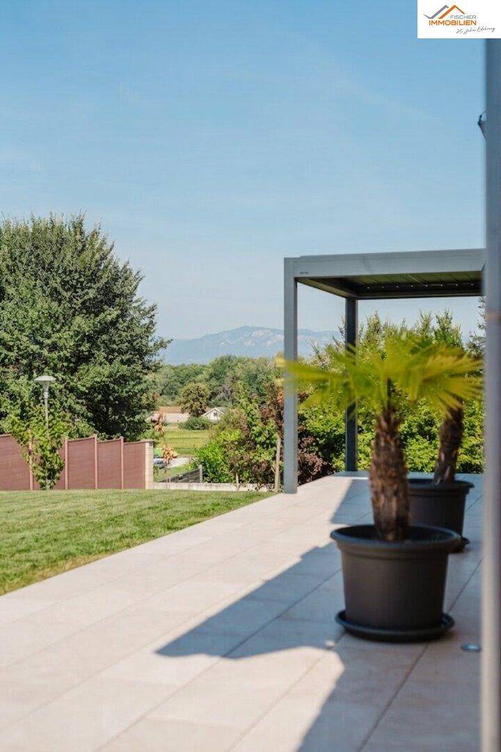 Helle Terrasse mit Pergola, Topfpflanzen und weitem Blick auf die umliegende Landschaft und Berge.