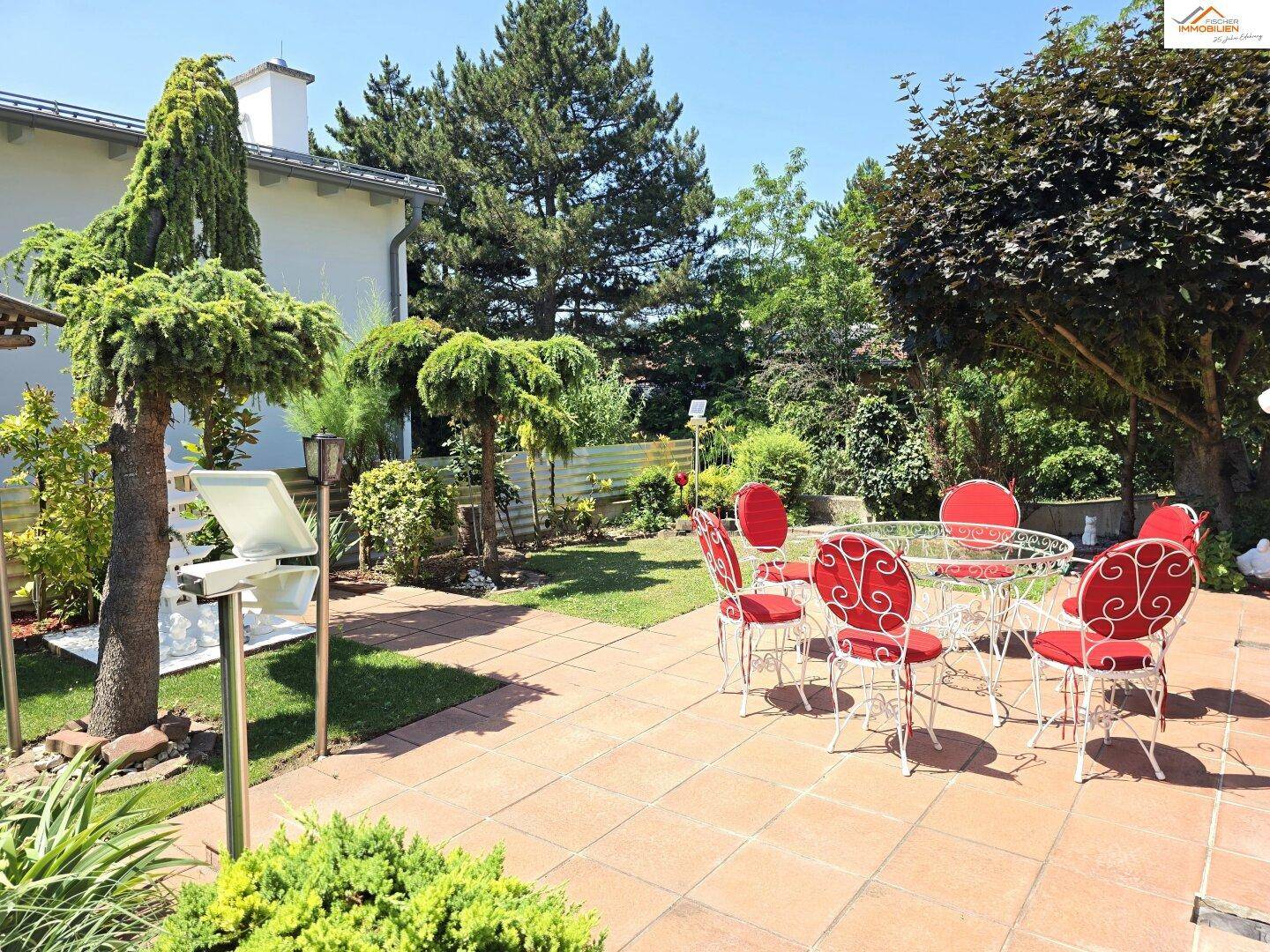 Gepflegter Garten mit großer Terrasse und Gartenmöbeln, umgeben von üppiger Vegetation.