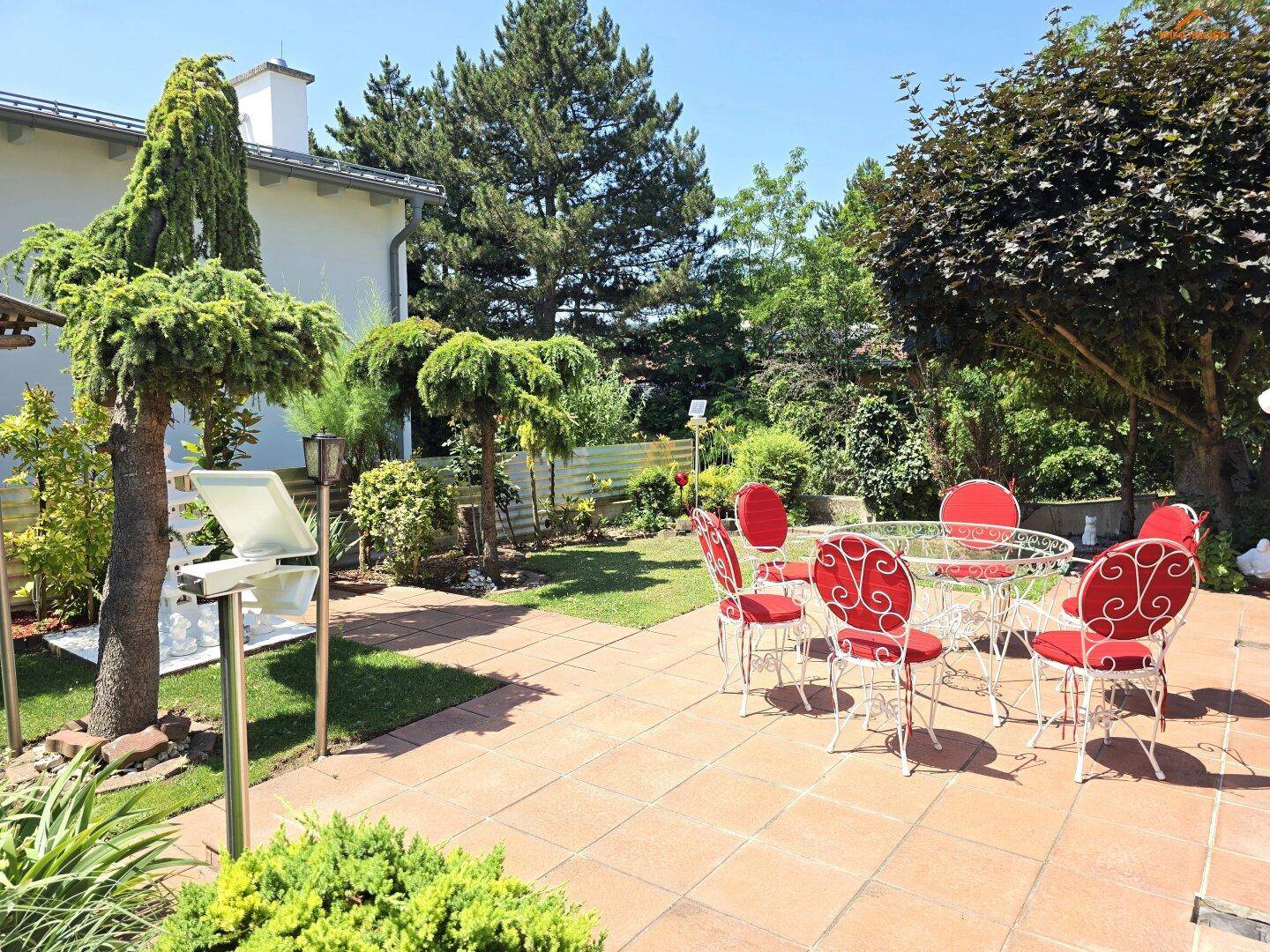 Weitläufiger Garten mit Terrasse, Gartenmöbeln und dekorativen Bäumen unter blauem Himmel.