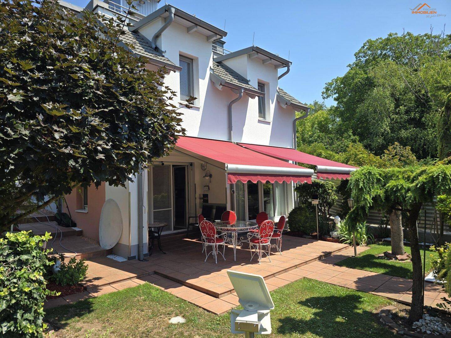 Große Terrasse mit Gartenmöbeln und roter Markise, umgeben von einem gepflegten Garten.