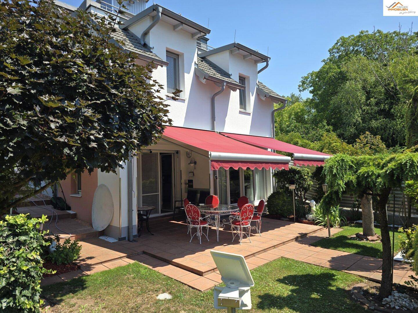 Weitläufige Terrasse mit roter Markise und Gartenblick, ideal für entspannte Stunden im Freien.