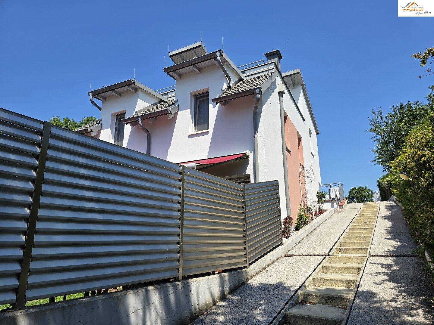 Rückansicht des Hauses mit moderner Zaunanlage und Zugang über eine Außentreppe.