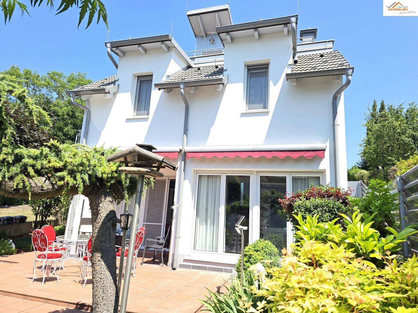Sonniger Terrassenbereich mit Gartenmöbeln und üppiger Bepflanzung, ideal für Mahlzeiten im Freien.