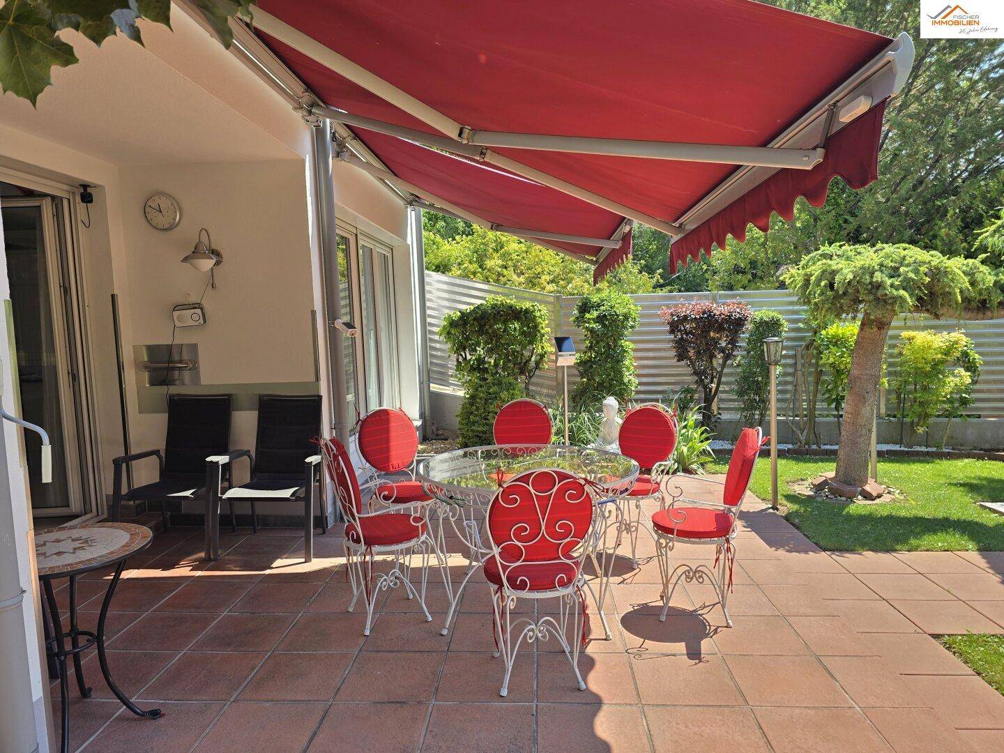 Überdachte Terrasse mit roter Markise und Gartenmöbeln, bietet Schutz vor Sonne und Regen.