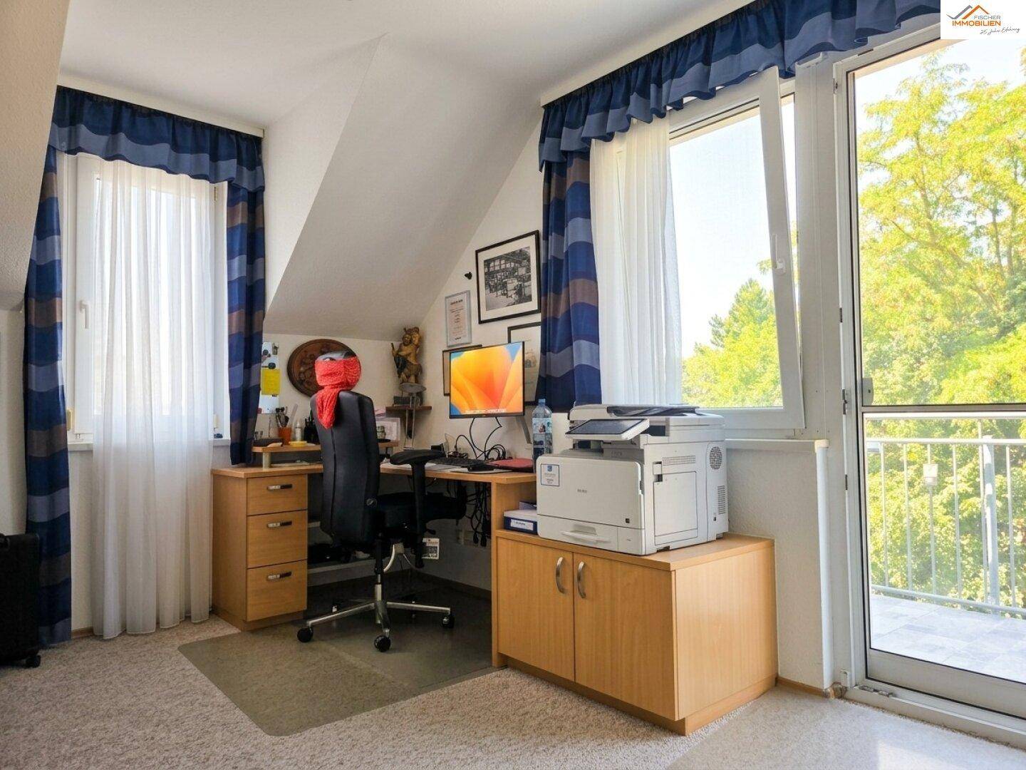 Gemütliches Arbeitszimmer mit Dachschräge und Zugang zu einem kleinen Balkon mit grüner Aussicht.