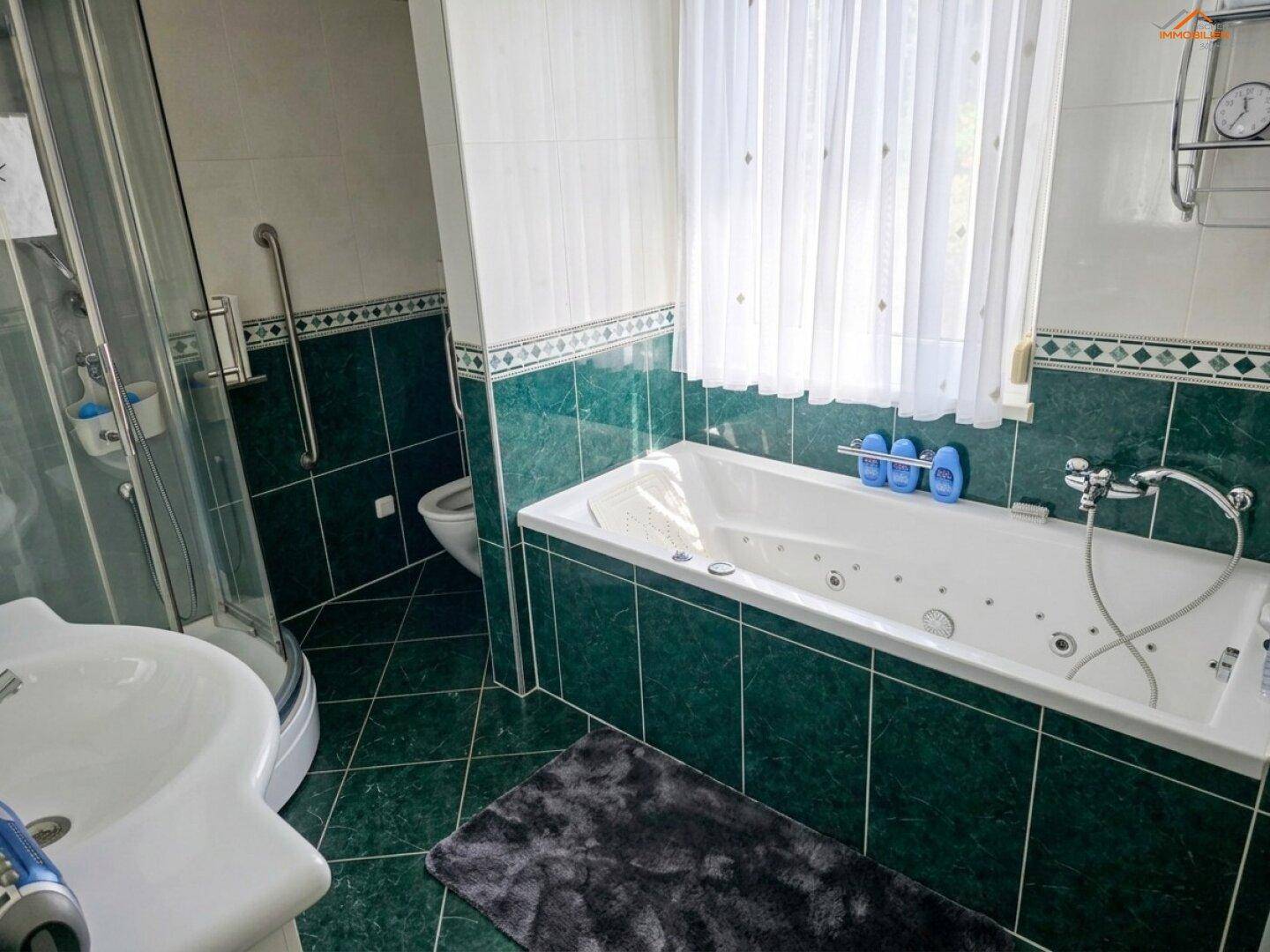 Badezimmer mit grünen Fliesen, Badewanne mit Whirlpoolfunktion und separater Duschkabine.