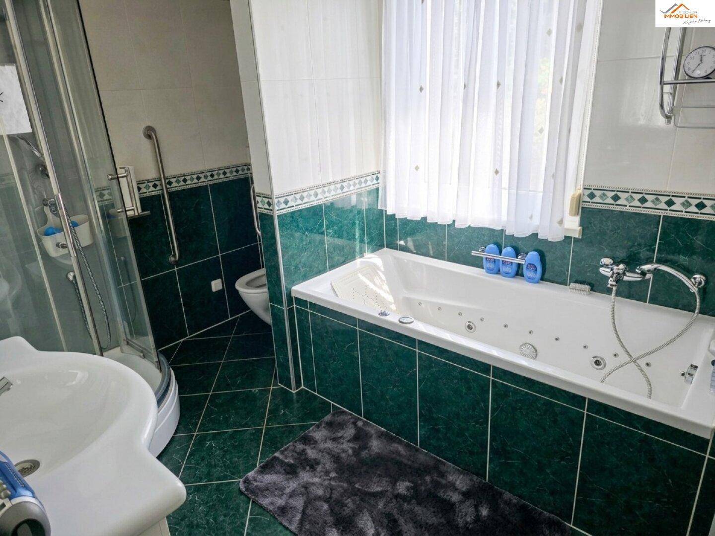 Badezimmer mit grünen Fliesen, Badewanne mit Whirlpoolfunktion und separater Dusche.