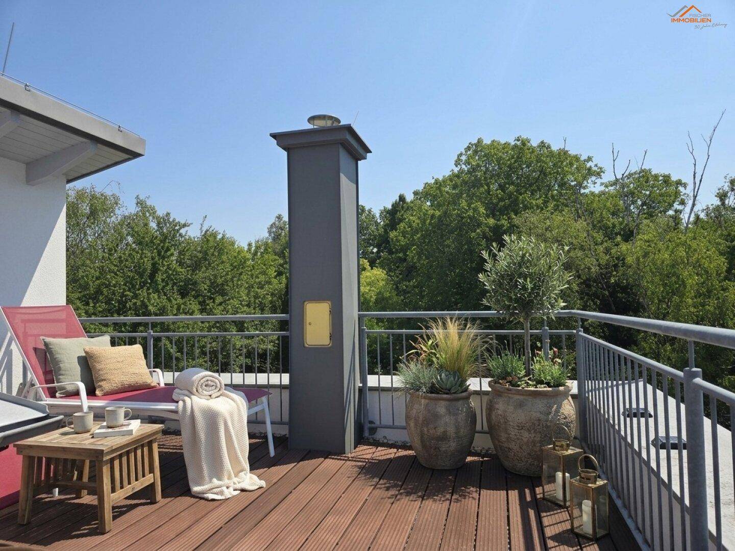 Sonnige Dachterrasse mit Holzbelag, Liegestuhl und dekorativen Pflanzen, umgeben von Bäumen.