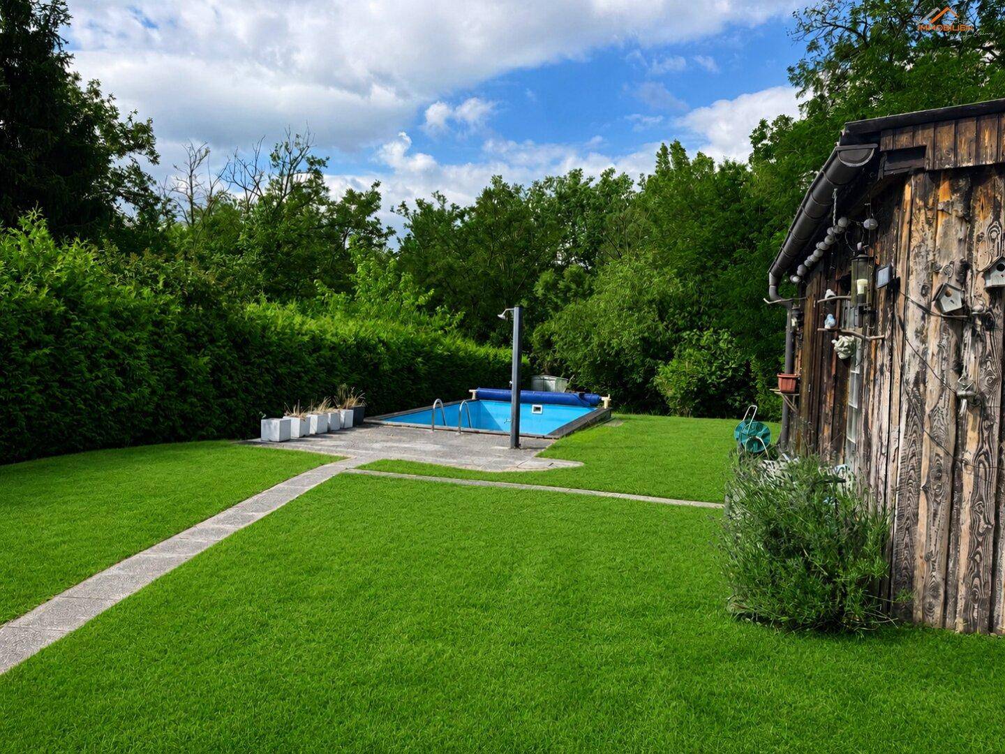 Grüner Garten mit eingelassenem Pool und rustikalem Holzschuppen unter blauem Himmel.