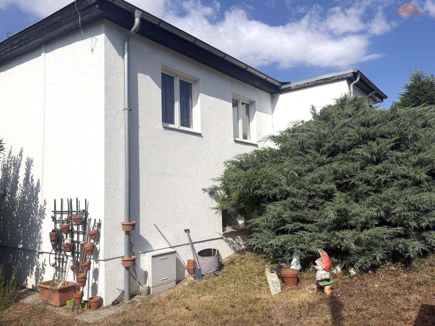 Seitenansicht des Hauses mit Büschen, Blumentöpfen und Gartenzwergen im Vorgarten.