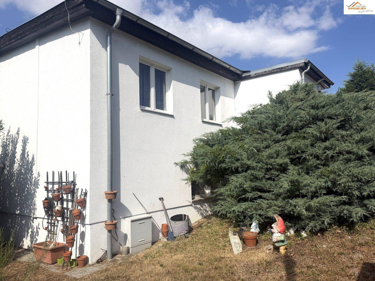 Seitenansicht des Hauses mit weißer Fassade, Fenstern und dekorativen Gartenzwergen.