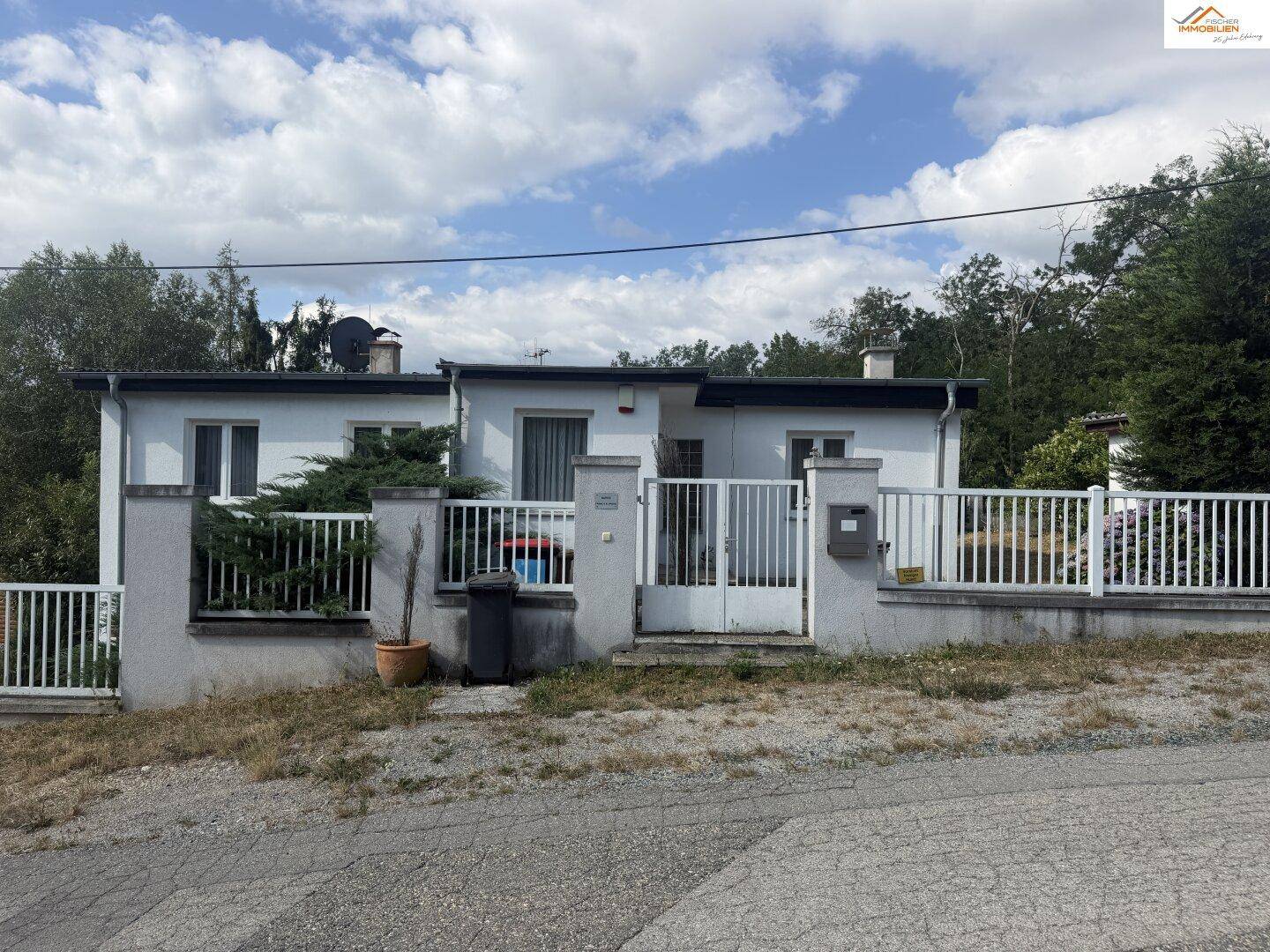 Vorderansicht des Hauses von der Straße aus, mit Zaun und Einfahrtstor.