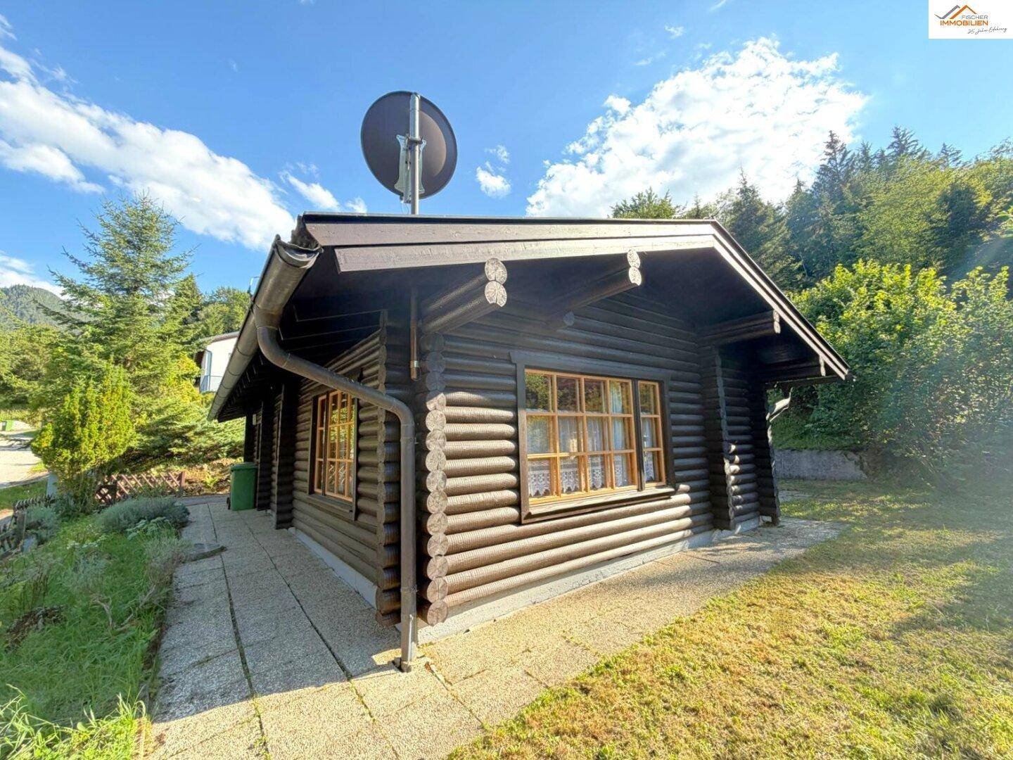 Seitenansicht des Blockhauses mit Holzfassade und einem gepflasterten Weg entlang des Gebäudes.