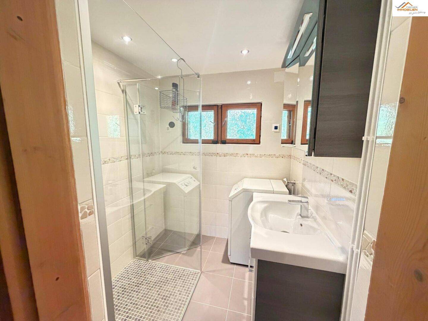 Modernes Badezimmer mit Duschkabine, Waschbecken und Waschmaschine, hell gefliest.
