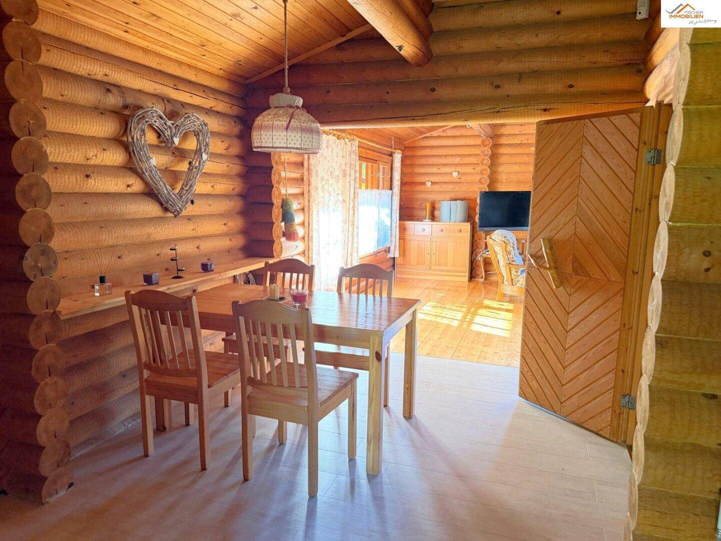 Rustikaler Essbereich im Blockhaus mit Holztisch und Stühlen, umgeben von warmen Holzwänden.