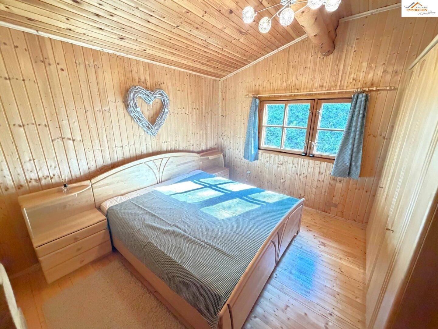 Helles Schlafzimmer im Blockhaus mit Holzbett, Nachttischen und vollständig holzvertäfelten Wänden und Decke.