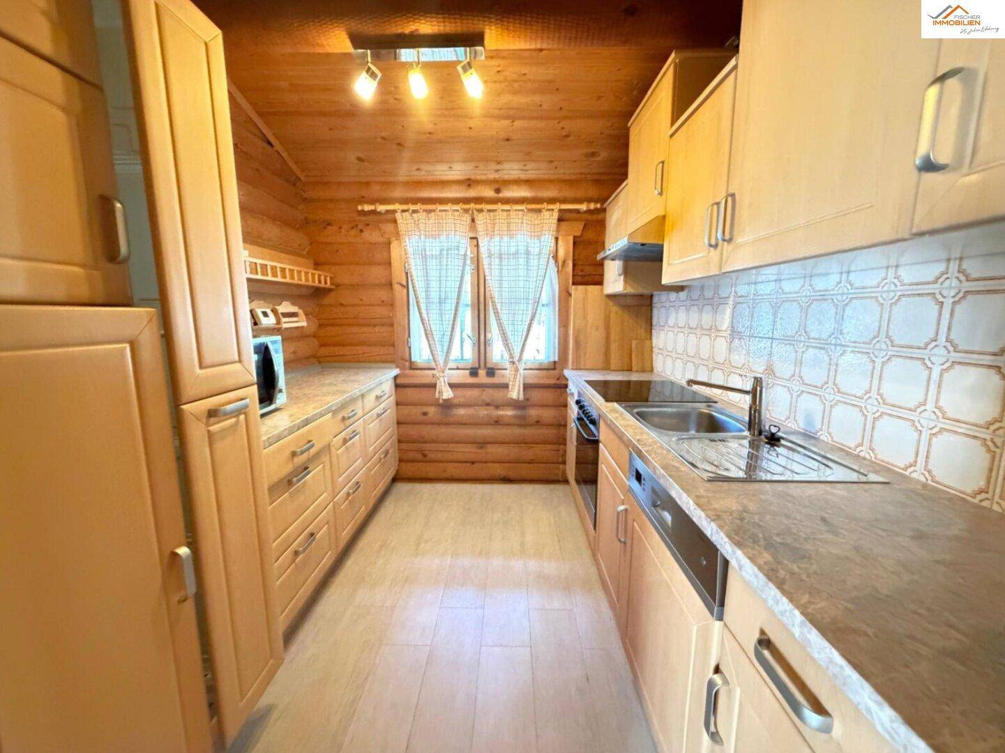 Gemütliche Küche im Blockhausstil mit Holzschränken, Arbeitsplatten in Steinoptik und Fenster.