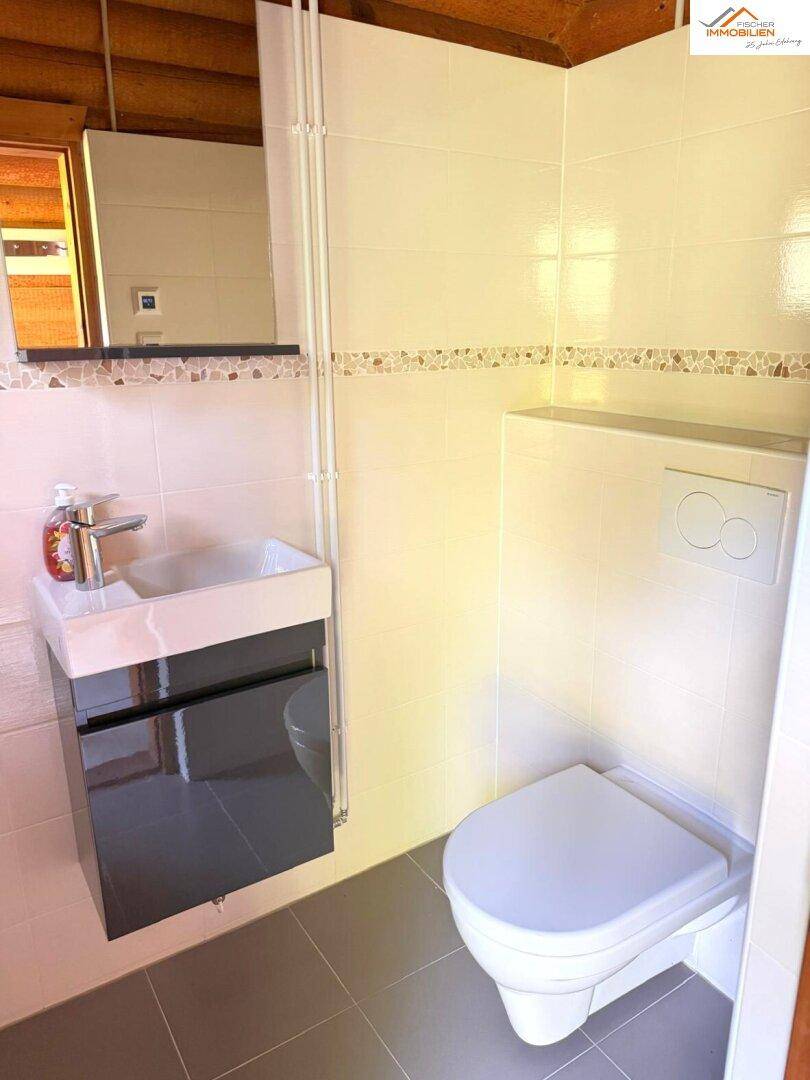 Kleines Badezimmer mit wandhängendem WC und modernem Waschbecken, hell gefliest.