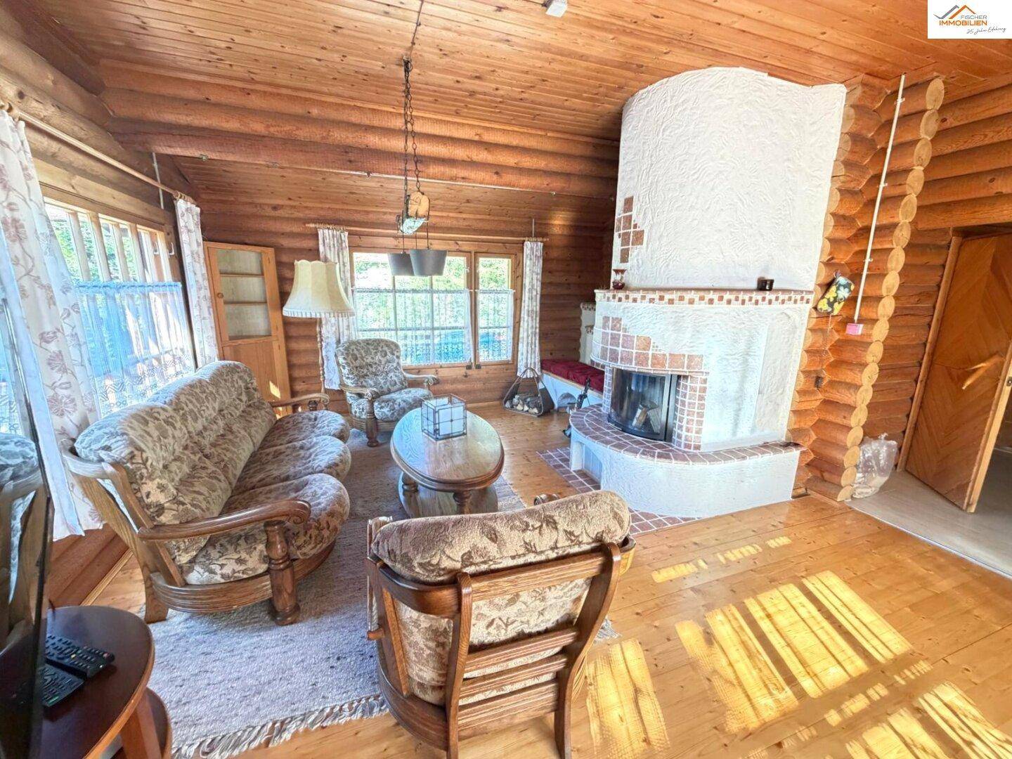 Geräumiges Wohnzimmer im Blockhaus mit Kamin, Sitzgelegenheiten und warmen Holzoberflächen.