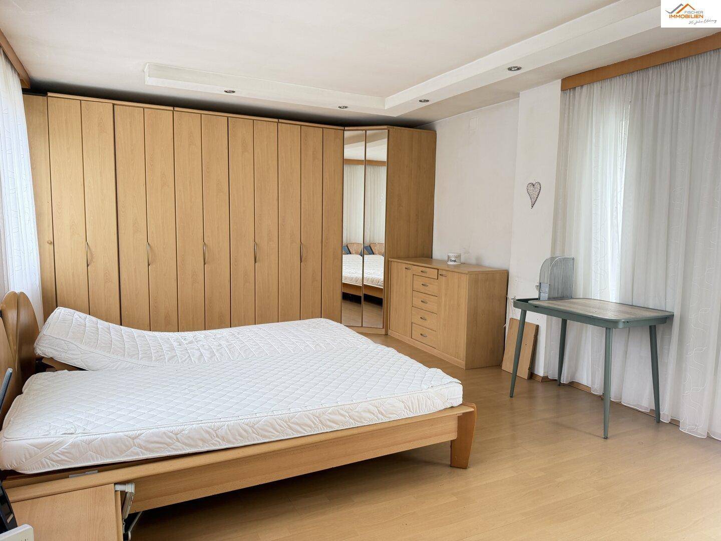 Geräumiges Schlafzimmer mit hellem Holzbett, großem Einbauschrank und Schreibtisch.