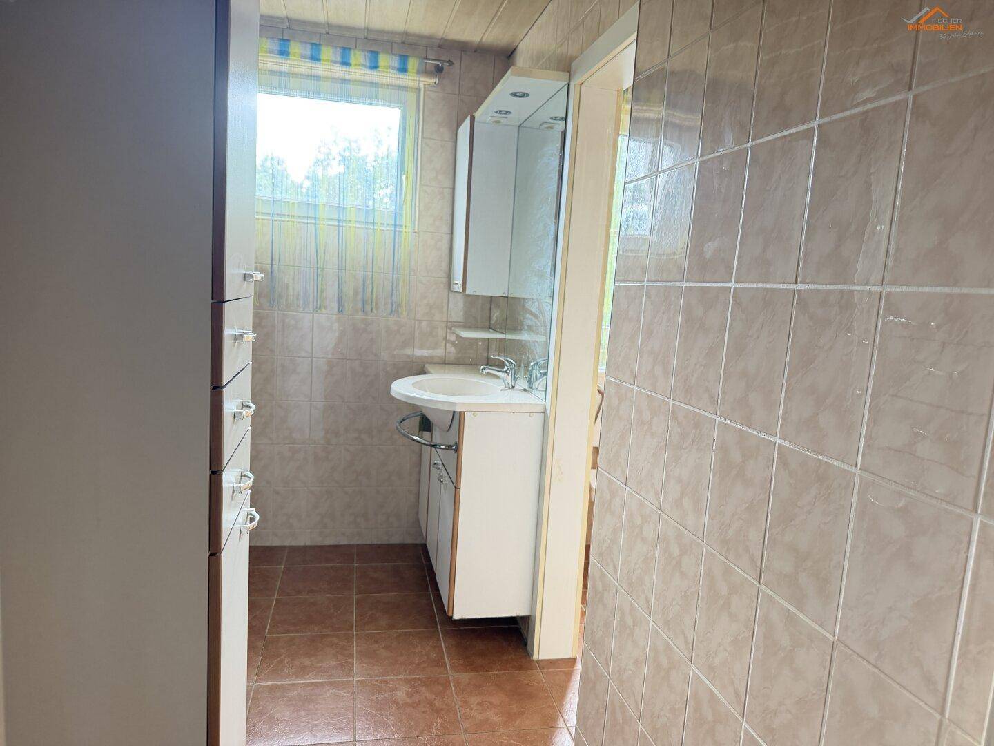 Gefliestes Badezimmer mit Waschbecken, Spiegelschrank und Fenster.