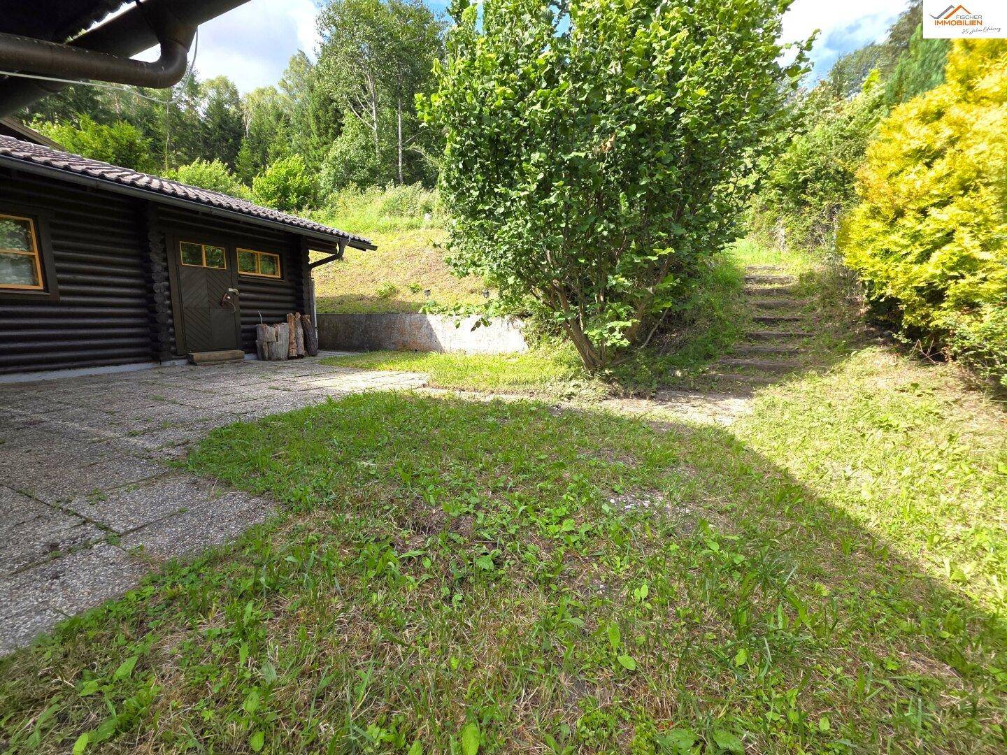 Gepflasterte Terrasse mit angrenzender Rasenfläche und Natursteintreppe zum oberen Gartenbereich.