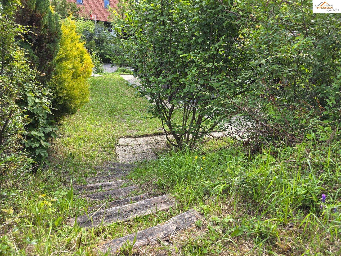 Grüner Gartenbereich mit rustikalen Holzstufen, die einen Hang hinaufführen, umgeben von Sträuchern.