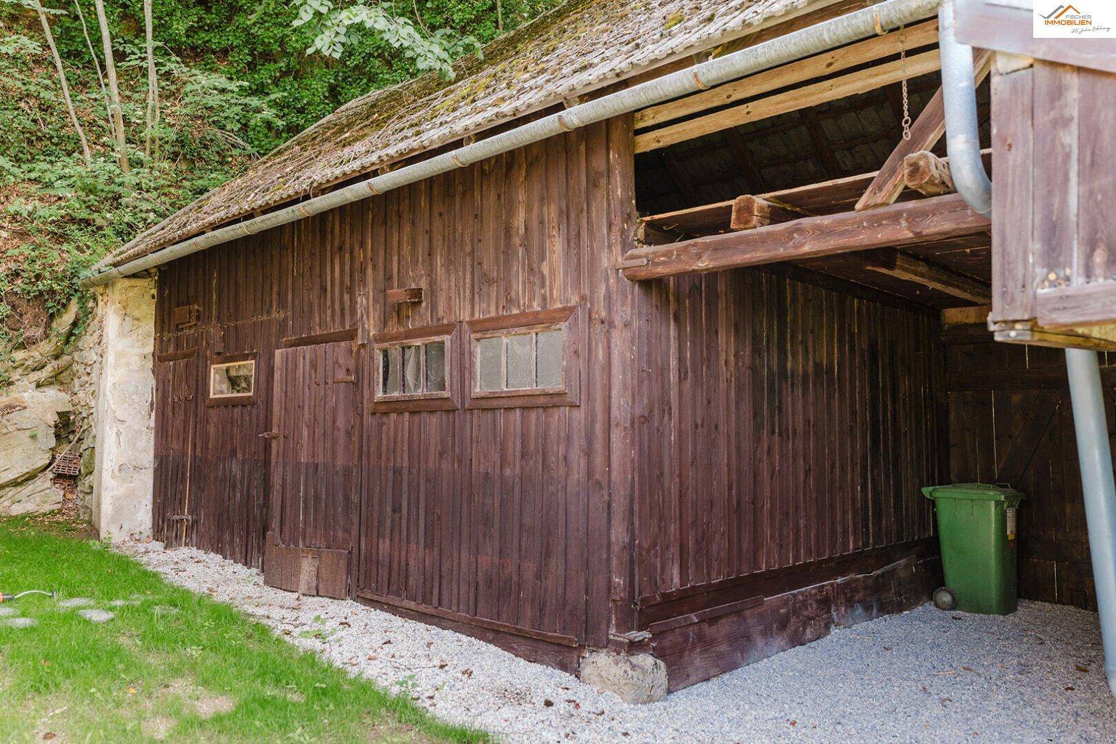 Rustikales Holzgebäude mit Schuppencharakter und Kiesweg im Grünen.