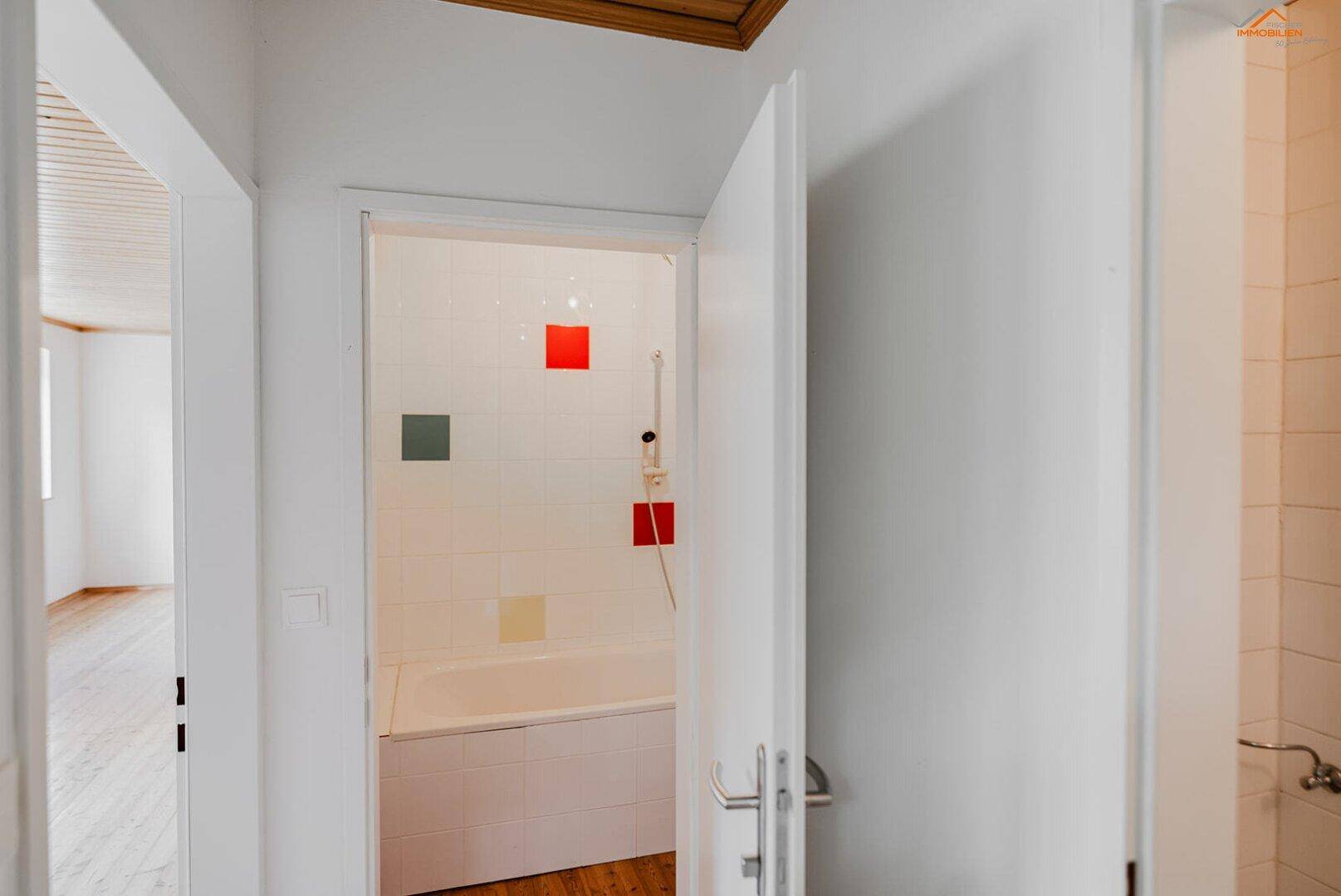 Badezimmer mit Badewanne, weißen Fliesen und farbigen Akzenten durch kleine Quadrate.