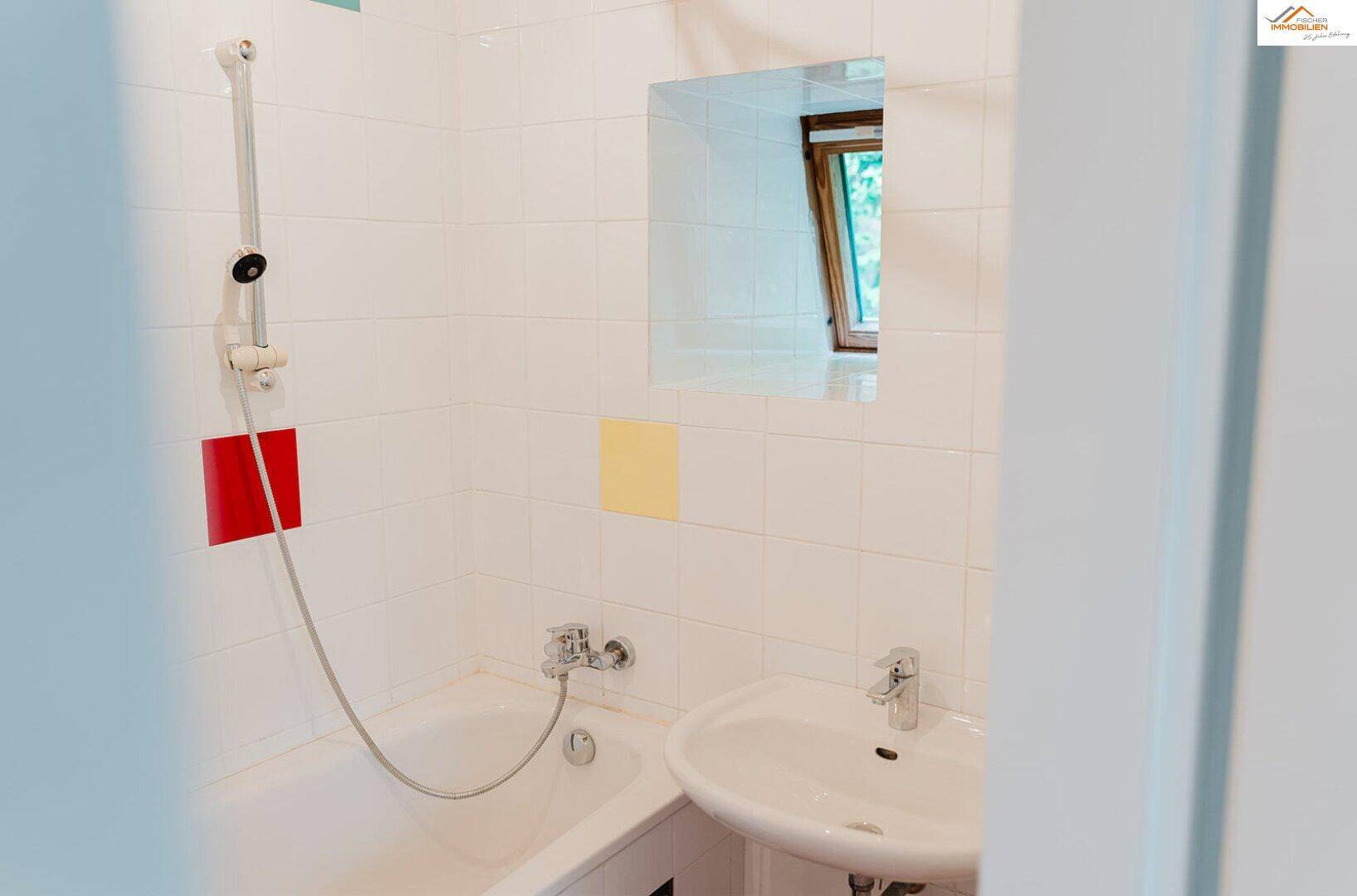 Badezimmer mit Badewanne, Waschbecken und bunten Fliesenakzenten.