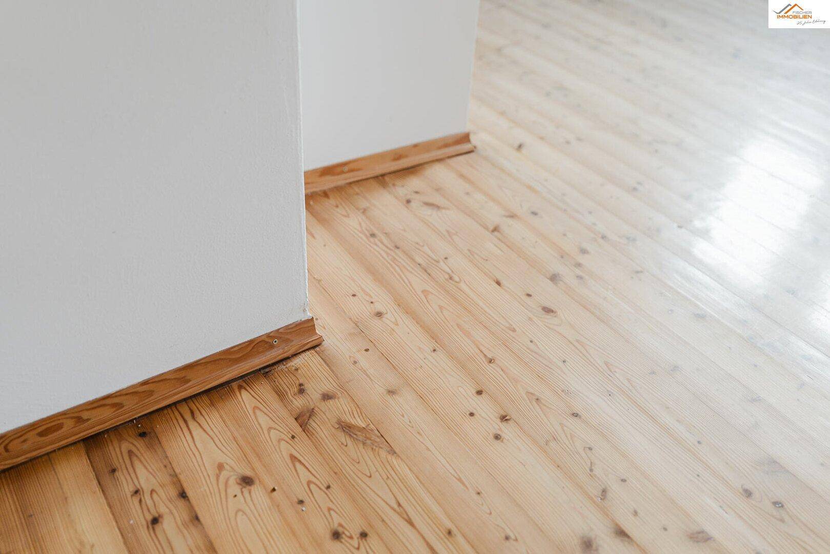 Detailansicht des hellen Holzplankenbodens mit Fußleisten in einem Innenraum.