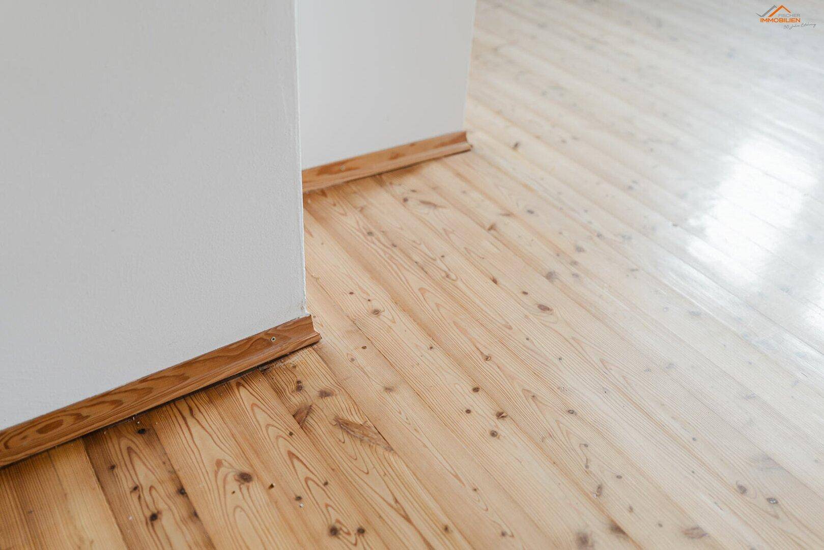 Detailansicht eines hellen Holzplankenbodens mit weißer Wand und Holzleiste.