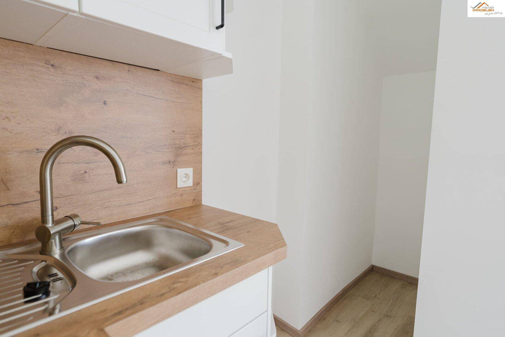 Detailansicht der Küchenzeile mit Spüle, Armatur und Arbeitsplatte in Holzoptik.