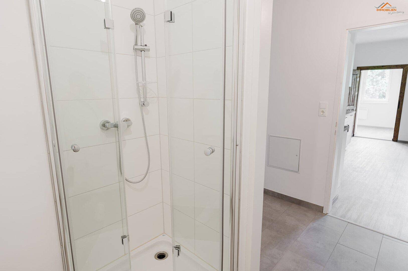 Helle Duschkabine mit weißen Fliesen und moderner Armatur in einem Badezimmer.