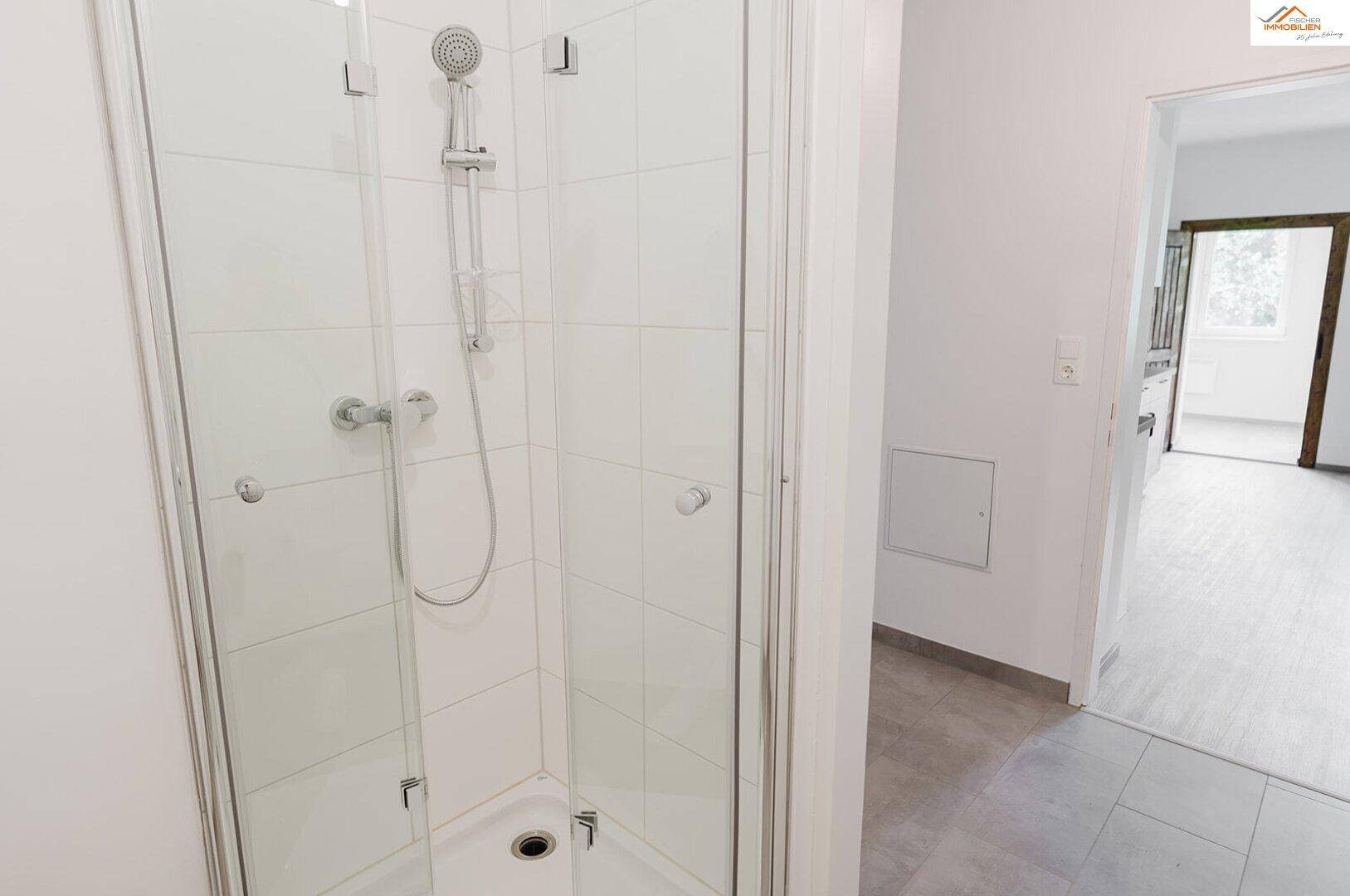 Duschkabine mit Glaswänden und weißen Fliesen in einem hellen Badezimmer.