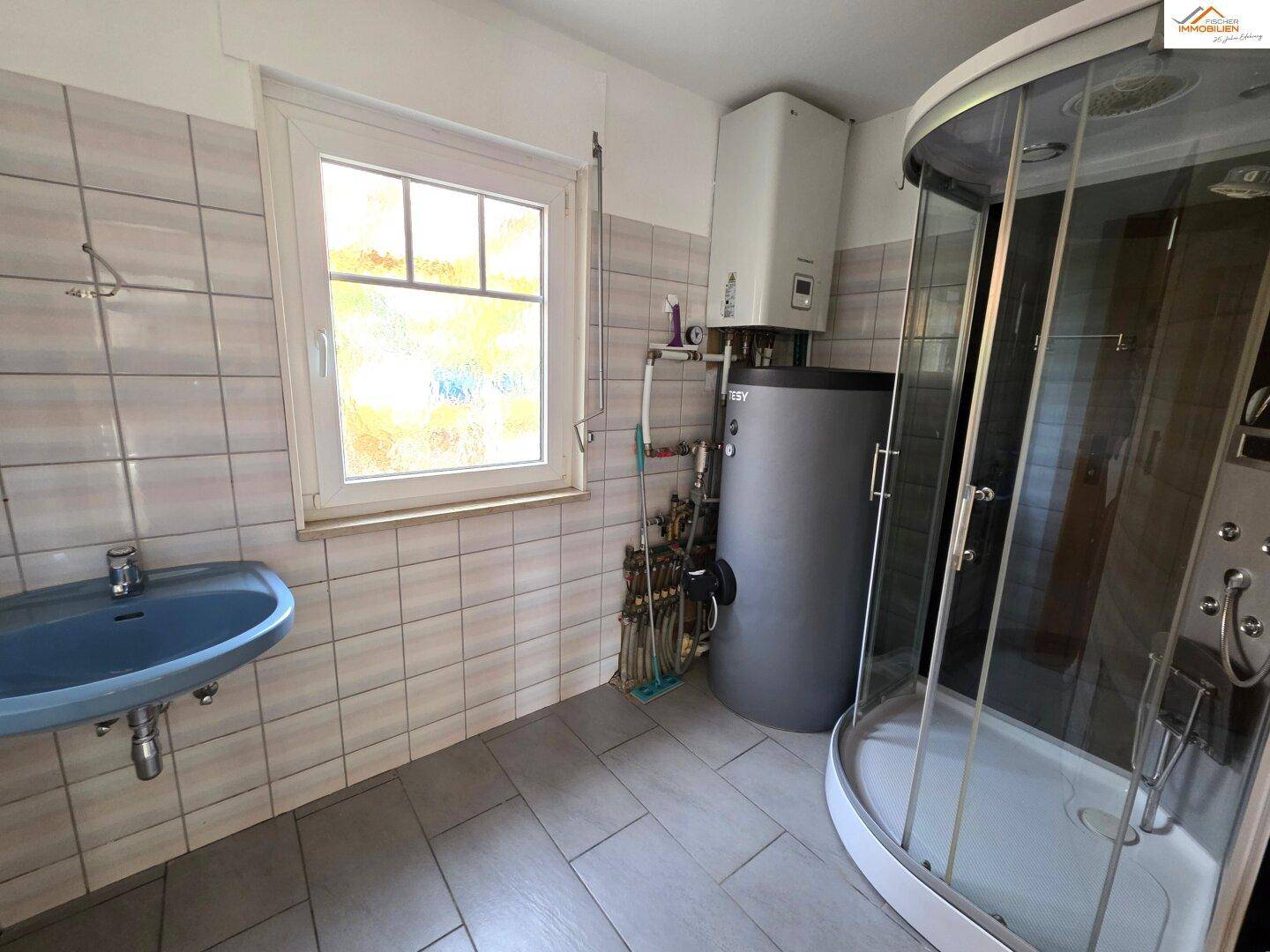 Einfaches Badezimmer mit Duschkabine, Waschbecken und Warmwasserboiler.