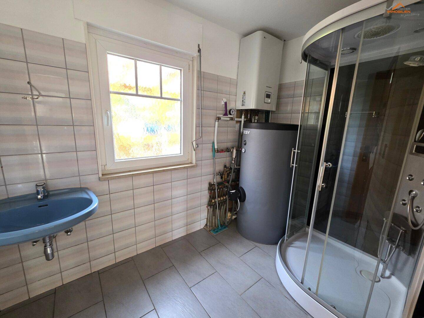 Hauswirtschaftsraum mit Duschkabine, Waschbecken und Warmwasserboiler.