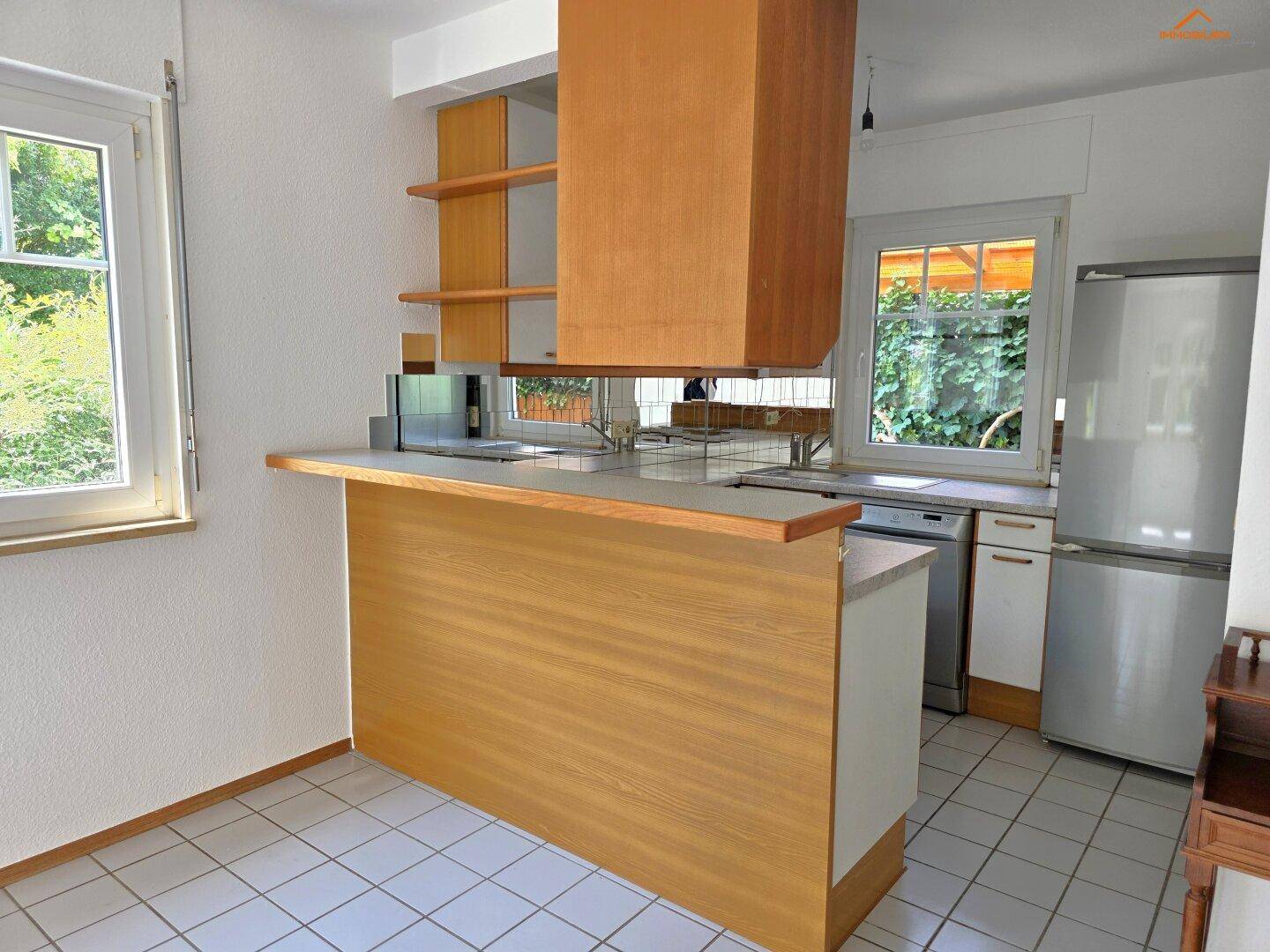Küche mit Frühstücksbar, Holzfronten und Blick ins Grüne durch das Fenster.