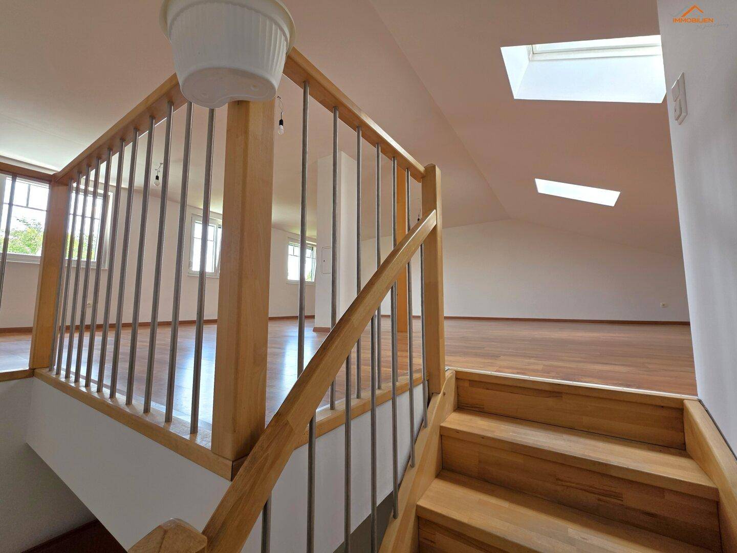 Holztreppe führt zu einem hellen Dachgeschoss mit Holzboden und Dachfenstern.