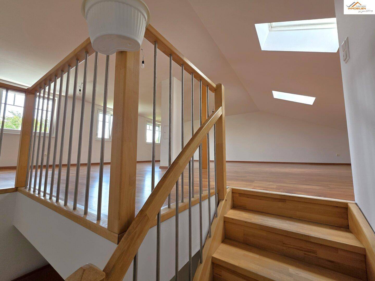 Holztreppe führt zu einem hellen Dachgeschossraum mit Holzboden und Dachfenstern.