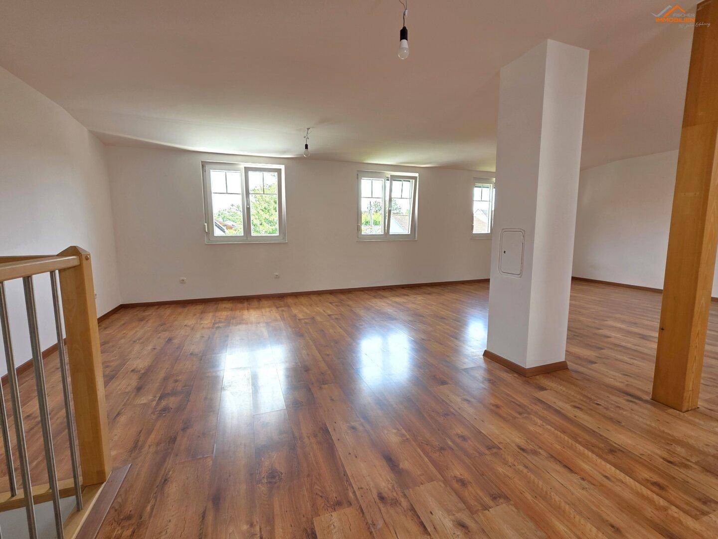 Geräumiges Dachgeschoss mit Holzboden, weißen Wänden und mehreren Fenstern.