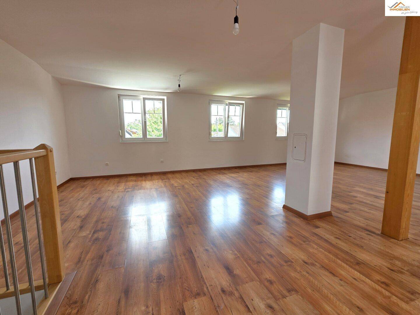 Geräumiger Dachgeschossraum mit Holzboden, weißen Wänden und mehreren Fenstern.