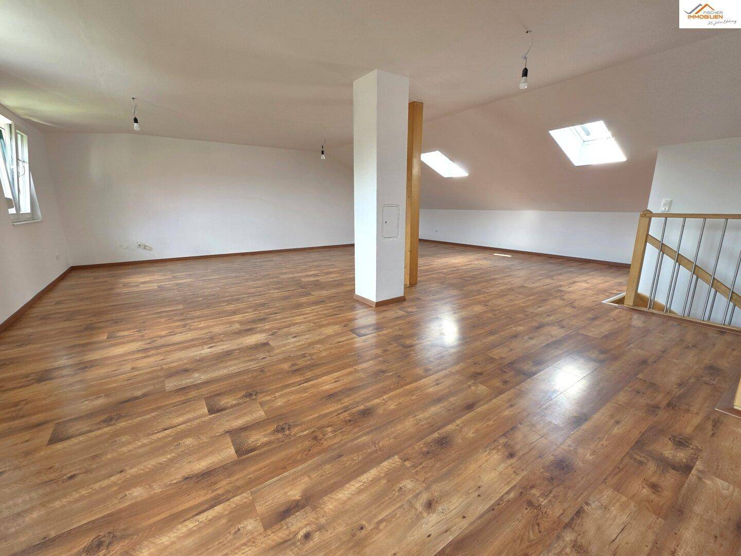 Heller und offener Dachgeschossraum mit Holzboden, Dachschrägen und Oberlichtern.